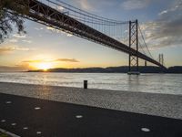 the golden hour lights up the sky near a long bridge over the water and a small area with squares on the ground in front