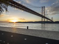 the golden hour lights up the sky near a long bridge over the water and a small area with squares on the ground in front