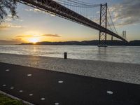 the golden hour lights up the sky near a long bridge over the water and a small area with squares on the ground in front