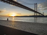 the golden hour lights up the sky near a long bridge over the water and a small area with squares on the ground in front