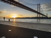 the golden hour lights up the sky near a long bridge over the water and a small area with squares on the ground in front