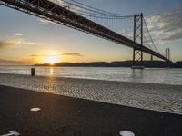 the golden hour lights up the sky near a long bridge over the water and a small area with squares on the ground in front