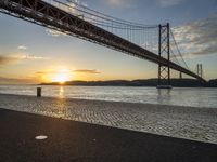 the golden hour lights up the sky near a long bridge over the water and a small area with squares on the ground in front