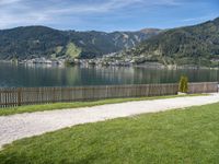 a green park bench sitting next to a lake and mountain view and grass covered pathway