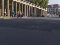 an empty street lined with pillars and a building in the back ground is a large group of people walking along it