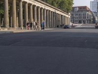 an empty street lined with pillars and a building in the back ground is a large group of people walking along it