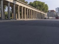 an empty street lined with pillars and a building in the back ground is a large group of people walking along it