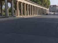 an empty street lined with pillars and a building in the back ground is a large group of people walking along it