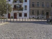 a man is walking through the street on the sidewalk next to buildings and trees in a cobblestone street