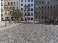 a man is walking through the street on the sidewalk next to buildings and trees in a cobblestone street