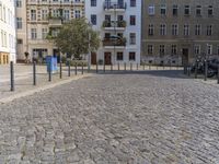 a man is walking through the street on the sidewalk next to buildings and trees in a cobblestone street