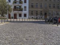 a man is walking through the street on the sidewalk next to buildings and trees in a cobblestone street