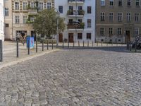 a man is walking through the street on the sidewalk next to buildings and trees in a cobblestone street