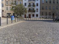 a man is walking through the street on the sidewalk next to buildings and trees in a cobblestone street