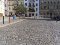 a man is walking through the street on the sidewalk next to buildings and trees in a cobblestone street