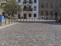 a man is walking through the street on the sidewalk next to buildings and trees in a cobblestone street