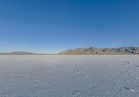 the lone man is walking across a salt plain in winter time in the desert with mountains in the distance