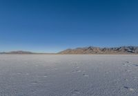 the lone man is walking across a salt plain in winter time in the desert with mountains in the distance