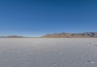 the lone man is walking across a salt plain in winter time in the desert with mountains in the distance