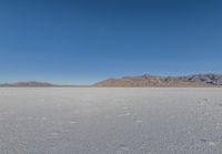 the lone man is walking across a salt plain in winter time in the desert with mountains in the distance