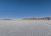 the lone man is walking across a salt plain in winter time in the desert with mountains in the distance