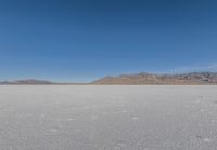 the lone man is walking across a salt plain in winter time in the desert with mountains in the distance