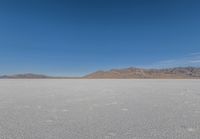 the lone man is walking across a salt plain in winter time in the desert with mountains in the distance