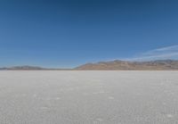 the lone man is walking across a salt plain in winter time in the desert with mountains in the distance