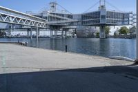 a man walking across a bridge over a river next to some buildings and cars under a bridge