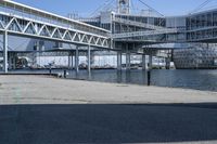 a man walking across a bridge over a river next to some buildings and cars under a bridge