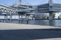 a man walking across a bridge over a river next to some buildings and cars under a bridge