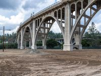 a large bridge over the dirt ground under a cloudy sky above a street corner in downtown area