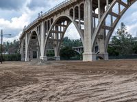 a large bridge over the dirt ground under a cloudy sky above a street corner in downtown area