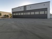 large hangar with a truck sitting outside of it on an empty lot in front of two buildings