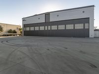 large hangar with a truck sitting outside of it on an empty lot in front of two buildings