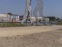 large metal sculptures of people facing each other on dirt path next to building complex with large metal structures in background