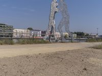 large metal sculptures of people facing each other on dirt path next to building complex with large metal structures in background