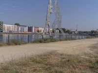 large metal sculptures of people facing each other on dirt path next to building complex with large metal structures in background