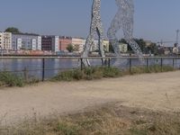 large metal sculptures of people facing each other on dirt path next to building complex with large metal structures in background