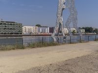 large metal sculptures of people facing each other on dirt path next to building complex with large metal structures in background