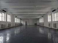 large open building with long floor space in middle of room with white walls and windows