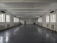 large open building with long floor space in middle of room with white walls and windows