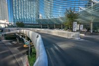 an empty street under a large bridge with glass buildings in the background with bicycle racks