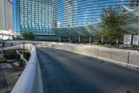 an empty street under a large bridge with glass buildings in the background with bicycle racks