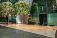 a large glass building with trees in front of it and sidewalk next to it on an outdoor space