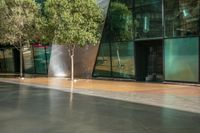 a large glass building with trees in front of it and sidewalk next to it on an outdoor space