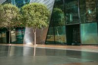 a large glass building with trees in front of it and sidewalk next to it on an outdoor space