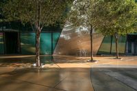 a group of trees sitting in front of a large building with large windows and a light reflecting off of it