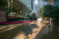 a statue of an elephant is in front of a tall glass building with trees and pink flowers