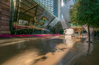 a statue of an elephant is in front of a tall glass building with trees and pink flowers